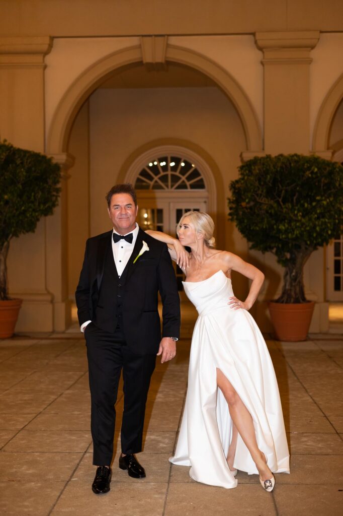 Bride leaning against groom in front of their wedding venue, the Ritz-Carlton in Naples, Florida