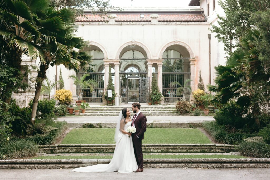 Bride and groom embrace during wedding portraits at an elegant outdoor Florida venue with Mediterranean-style arches and formal gardens, photographed during the best time of year to get married in Florida