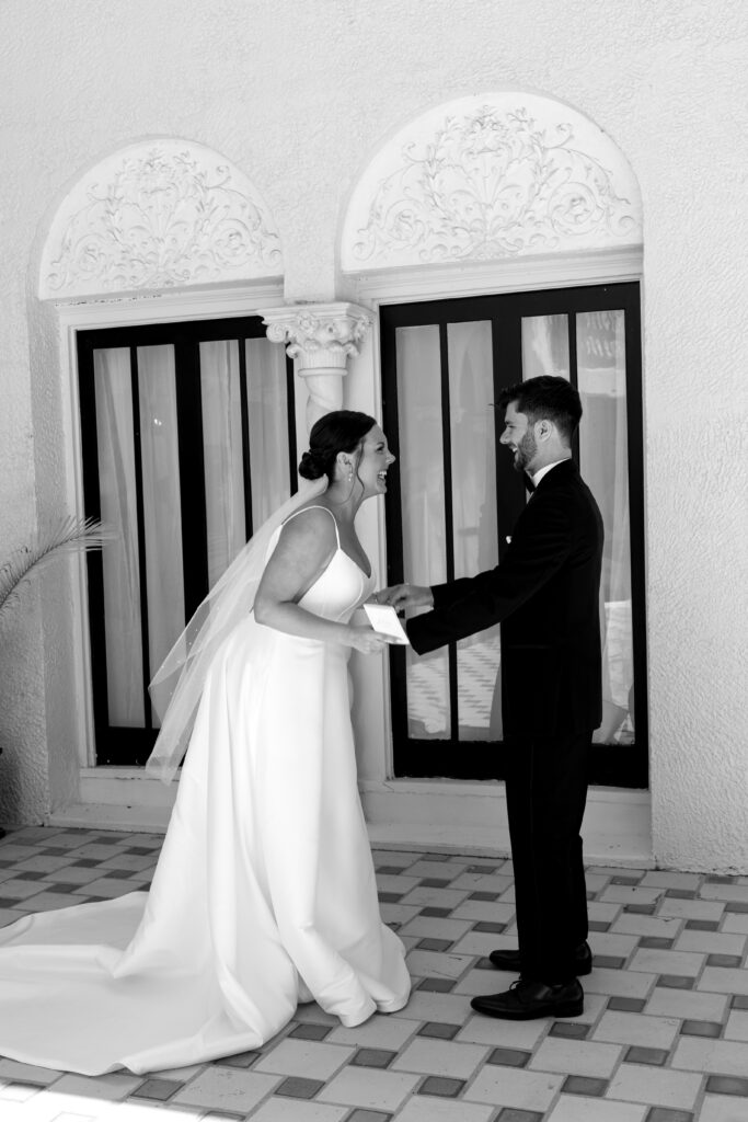 Bride and groom share a joyful first look outside a luxury Florida wedding venue, holding hands and smiling beneath ornate arches during one of the best months to get married outside in Florida