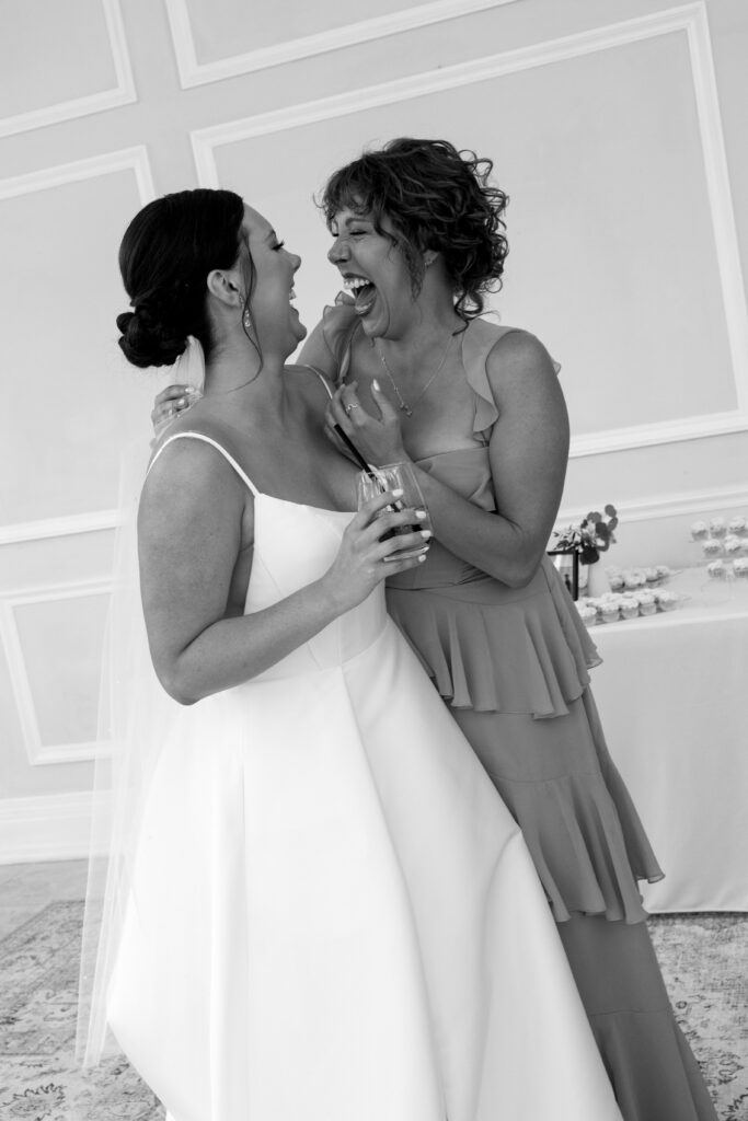 Bride laughs with a bridesmaid while holding a drink during, captured during the best time to get married in Florida.