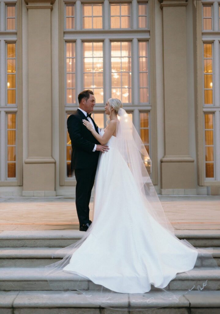 Elegant bride and groom share an intimate moment on grand stone steps outside a luxury Naples estate at sunset, showcasing a romantic outdoor celebration planned by experienced wedding planners in Naples Florida.