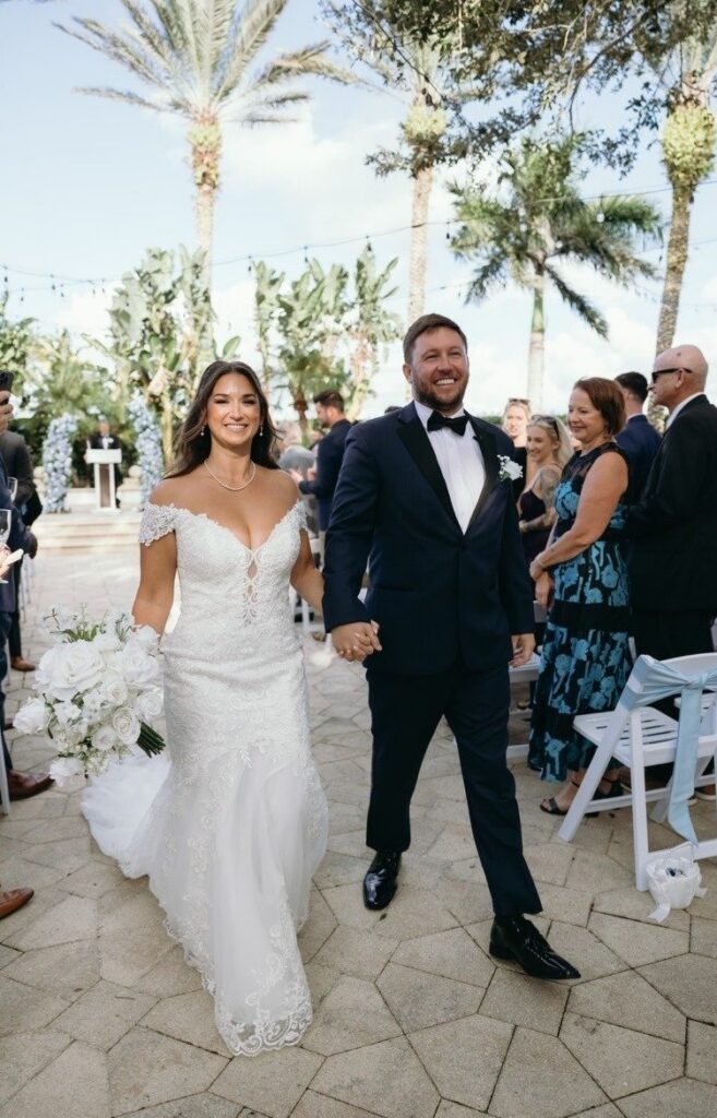 Newly married couple walks down the aisle during an outdoor Naples wedding celebration, surrounded by guests and tropical greenery, showcasing an elegant ceremony designed by experienced wedding planners Naples FL.