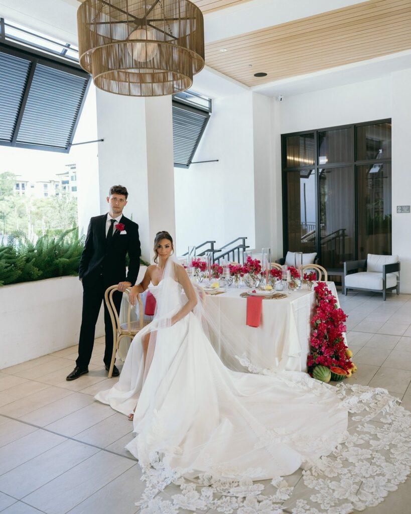 Bride and groom posing beside a romantic sweetheart table adorned with bold pink floral arrangements and contemporary décor at a luxury Naples FL wedding designed by professional wedding planners Naples Florida, captured by photographer Priscila del Cristo.