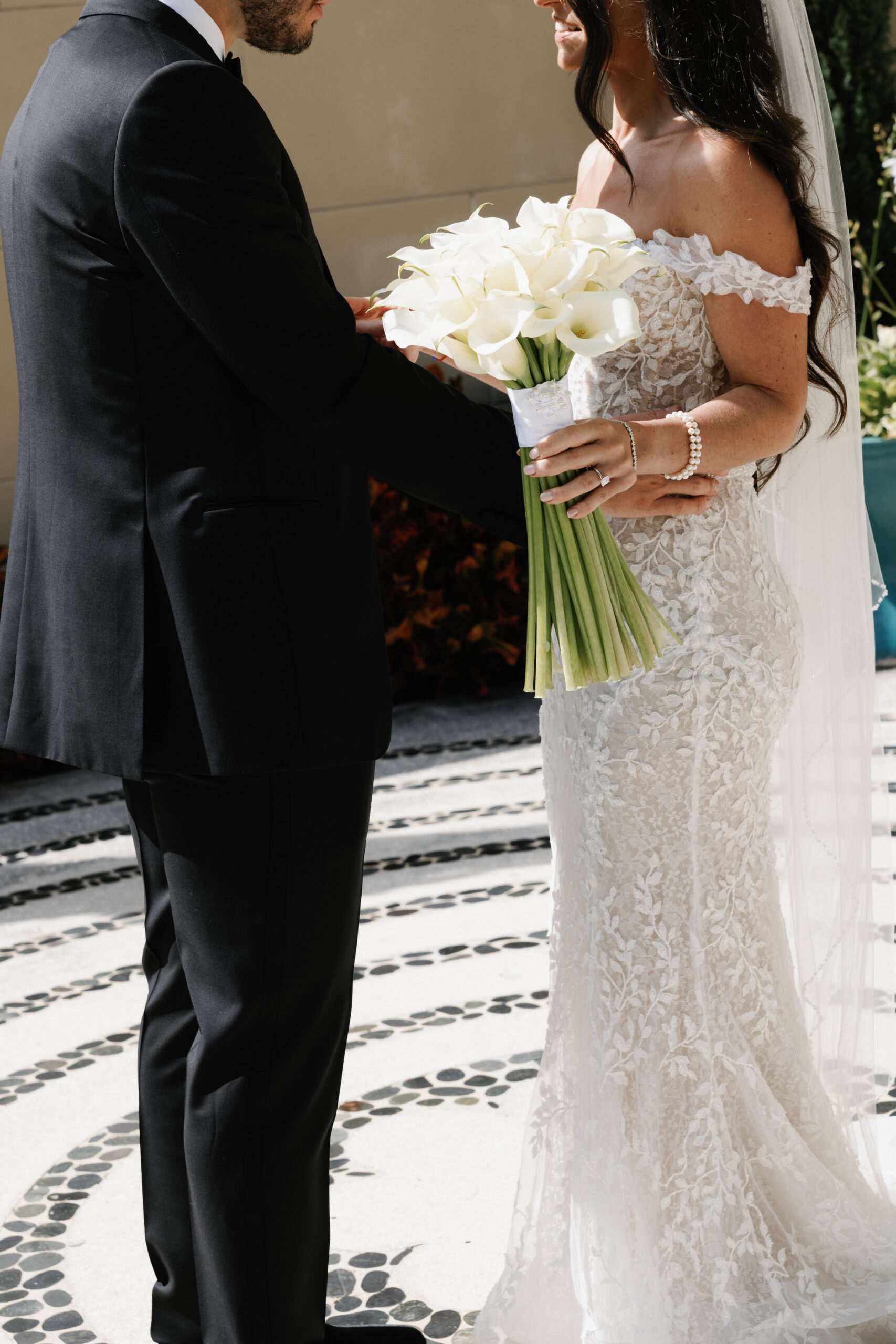crisp white floral bouquet in the hands of a bride and groom photographerd standing together at their wedding where floral arrangements were done by one of the best wedding florists in naples